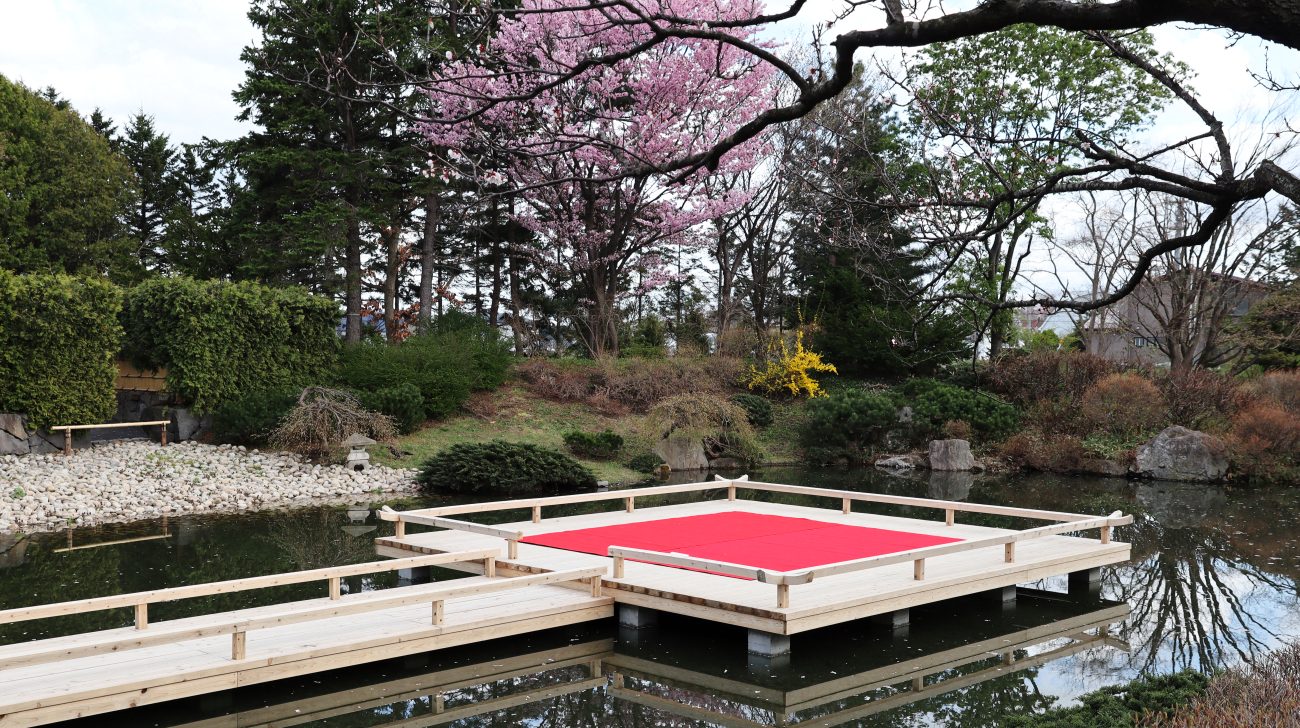 公園の池と浮き舞台、桜と木々(札幌市北区、2023年撮影)