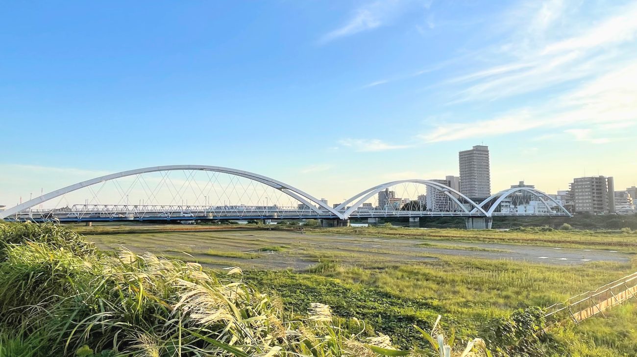 相模川の河川敷と白いアーチの橋、対岸の街並み（神奈川県海老名市、2021年撮影）
