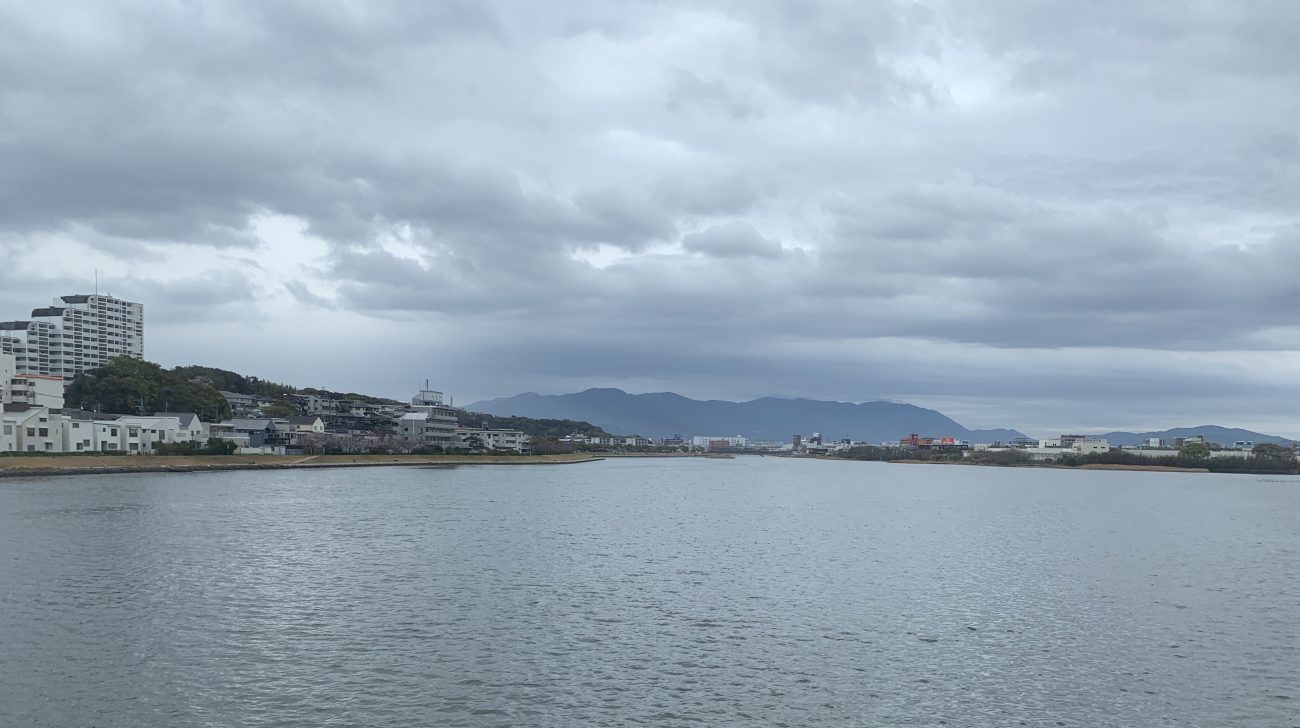 河口付近の川の水面と、対岸に並ぶ住宅や建物（福岡市東区、2021年撮影）